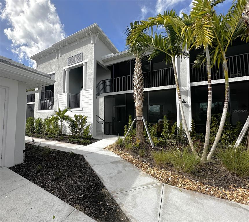 A two-story building exterior features a screened balcony, palm trees, and a concrete walkway — 14221 HERITAGE LANDING BOULEVARD UNIT 2014, PUNTA GORDA, FL