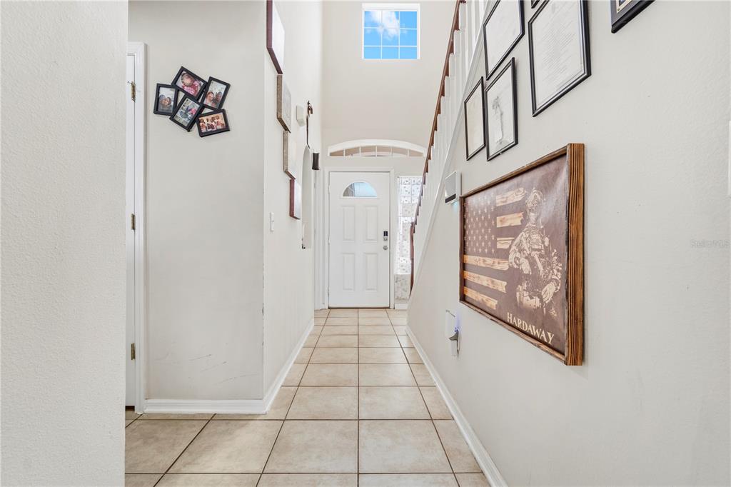 A tiled entryway features a staircase, a white front door, and wall-mounted picture frames — 2881 SW 142ND LANE, OCALA, FL