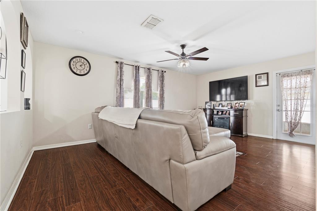 A living room features a grey sofa, dark wood flooring, a ceiling fan, and television — 2881 SW 142ND LANE, OCALA, FL