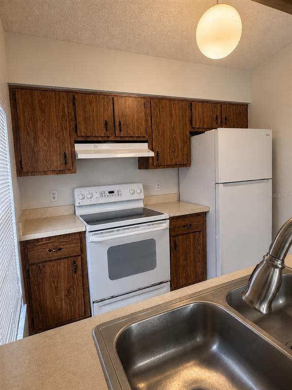 A kitchen features wood cabinets, white appliances, a double sink, and a pendant light — 3558 SW 157TH LOOP, OCALA, FL