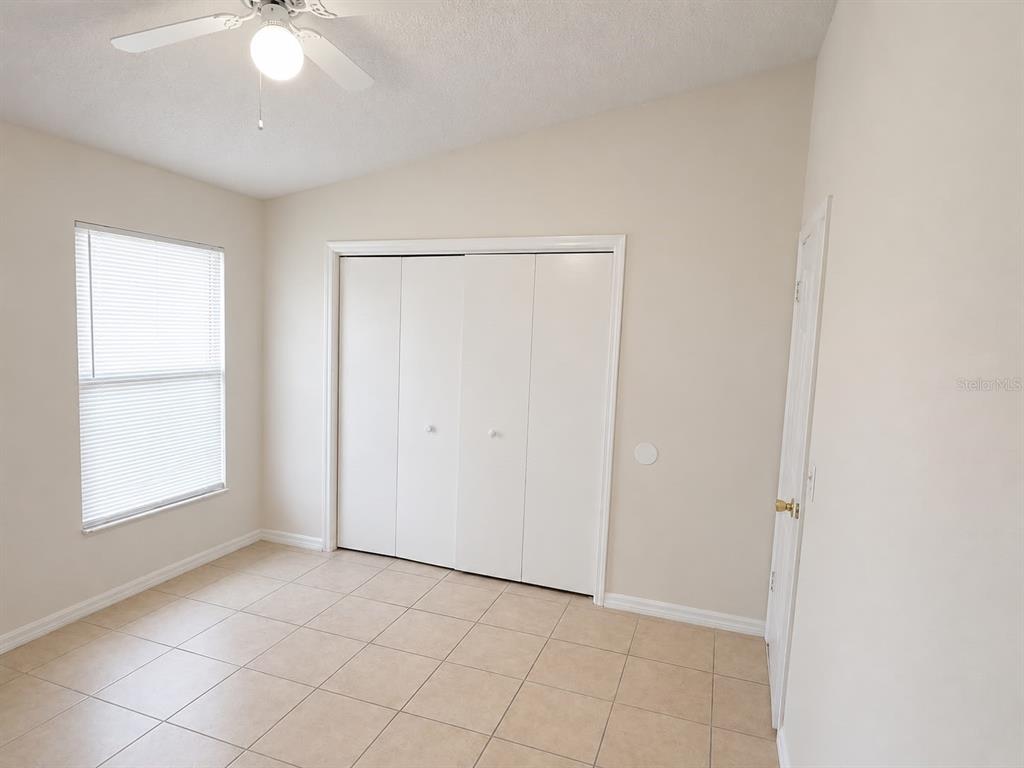 A bedroom with beige tile flooring, a ceiling fan, a window with blinds, and closets — 3558 SW 157TH LOOP, OCALA, FL
