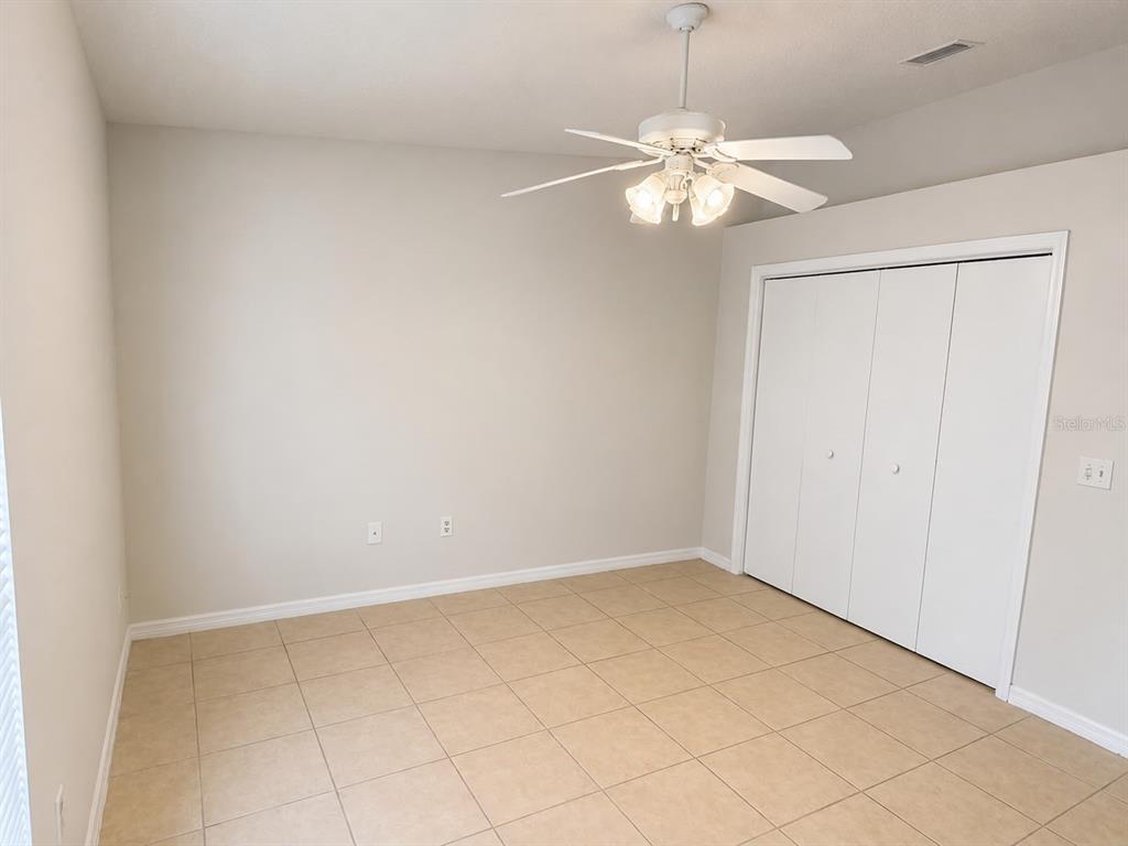 An empty room features beige tile flooring, light-colored walls, a ceiling fan, and white closet doors — 3558 SW 157TH LOOP, OCALA, FL