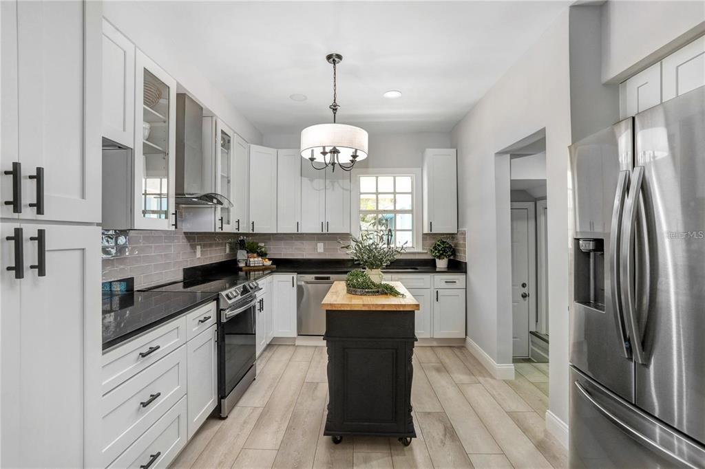 A kitchen features white cabinets, black countertops, a black rolling island, and light wood-look flooring — 1960 MCKINLEY STREET, CLEARWATER, FL