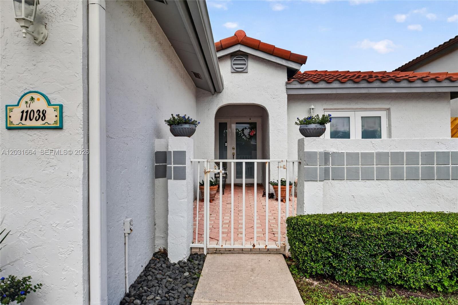 A white stucco house entrance features a gated courtyard, red tile roof, and address plaque — 11038 SW 148th Pl, Miami FL 33196, MIAMI, FL
