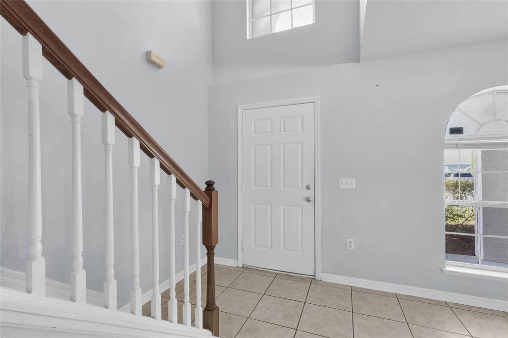An entryway features a tiled floor, a white front door, and a wooden staircase railing — 4125 SW 33RD STREET, OCALA, FL