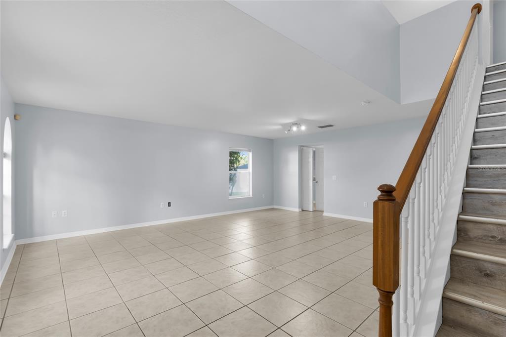 An empty room with light-colored tile flooring, pale blue walls, and a wooden staircase — 4125 SW 33RD STREET, OCALA, FL