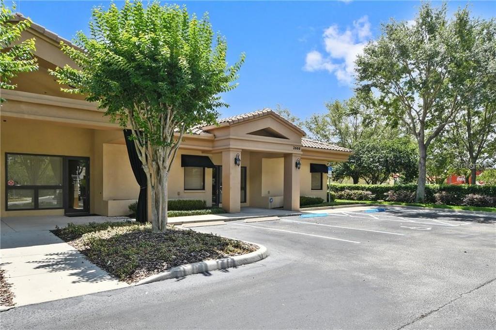 A tan commercial building with a covered entrance and parking lot under a blue sky — 2658 MAGUIRE ROAD, OCOEE, FL