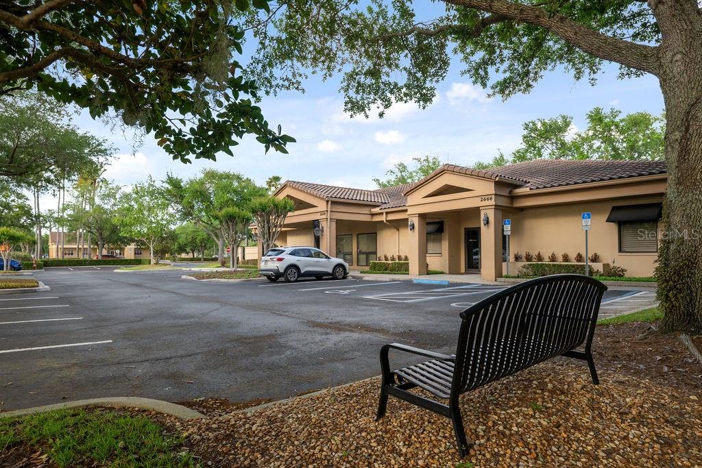 A black metal bench sits on a gravel patch in front of a commercial building — 2658 MAGUIRE ROAD, OCOEE, FL