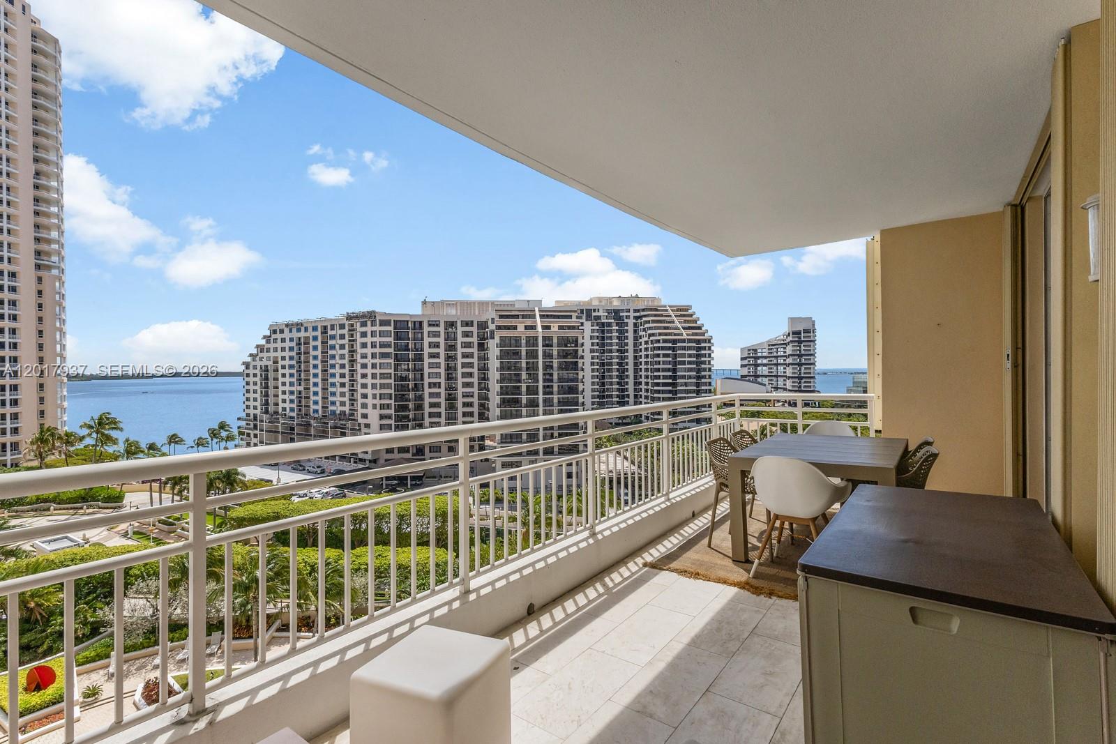 A balcony with tile flooring overlooks a bay, surrounding high-rise buildings, and landscaped grounds — 888 Brickell Key Dr # 1207, Miami FL 33131, MIAMI, FL