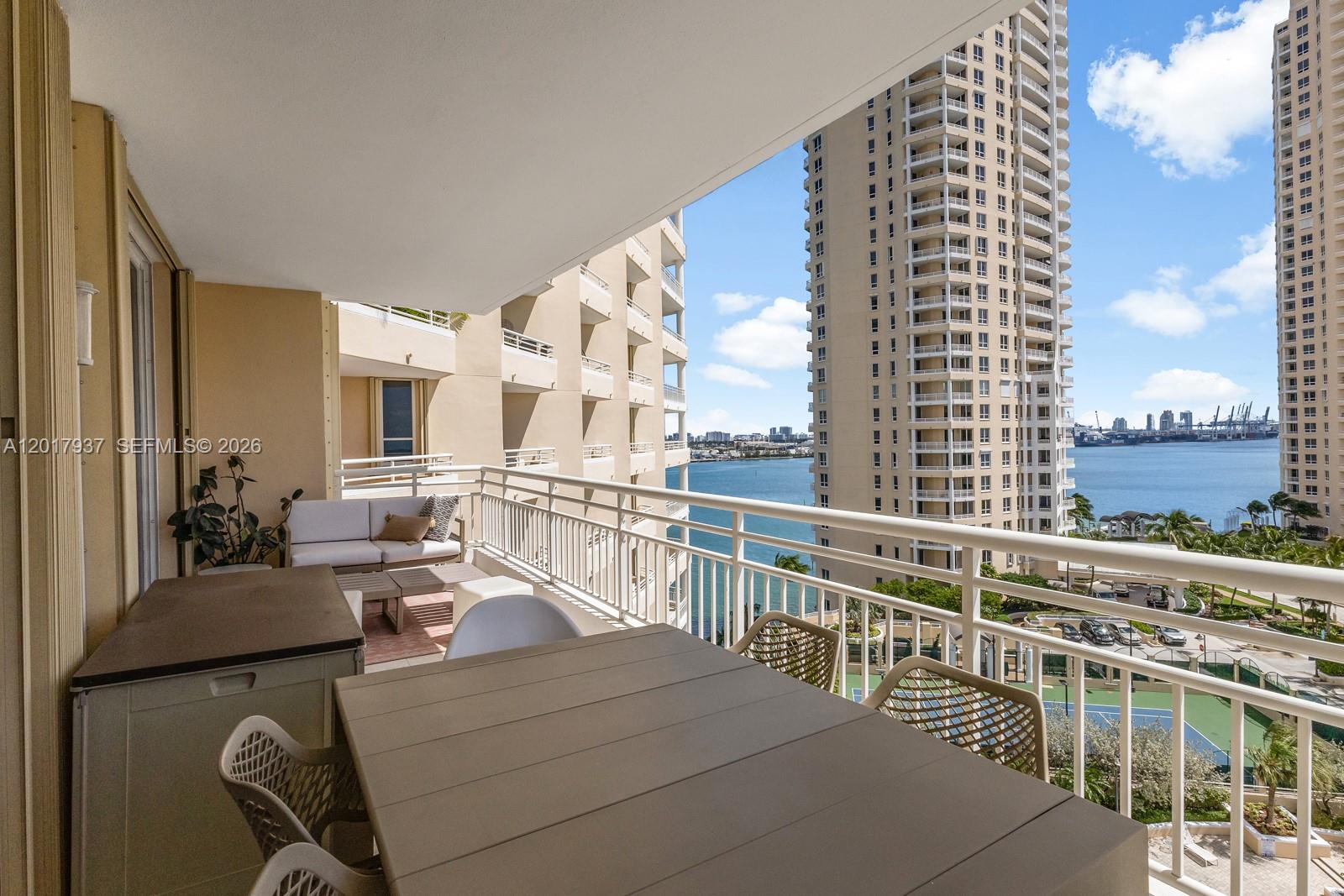 A balcony features a dining table, outdoor seating, and views of a bay and skyscrapers — 888 Brickell Key Dr # 1207, Miami FL 33131, MIAMI, FL