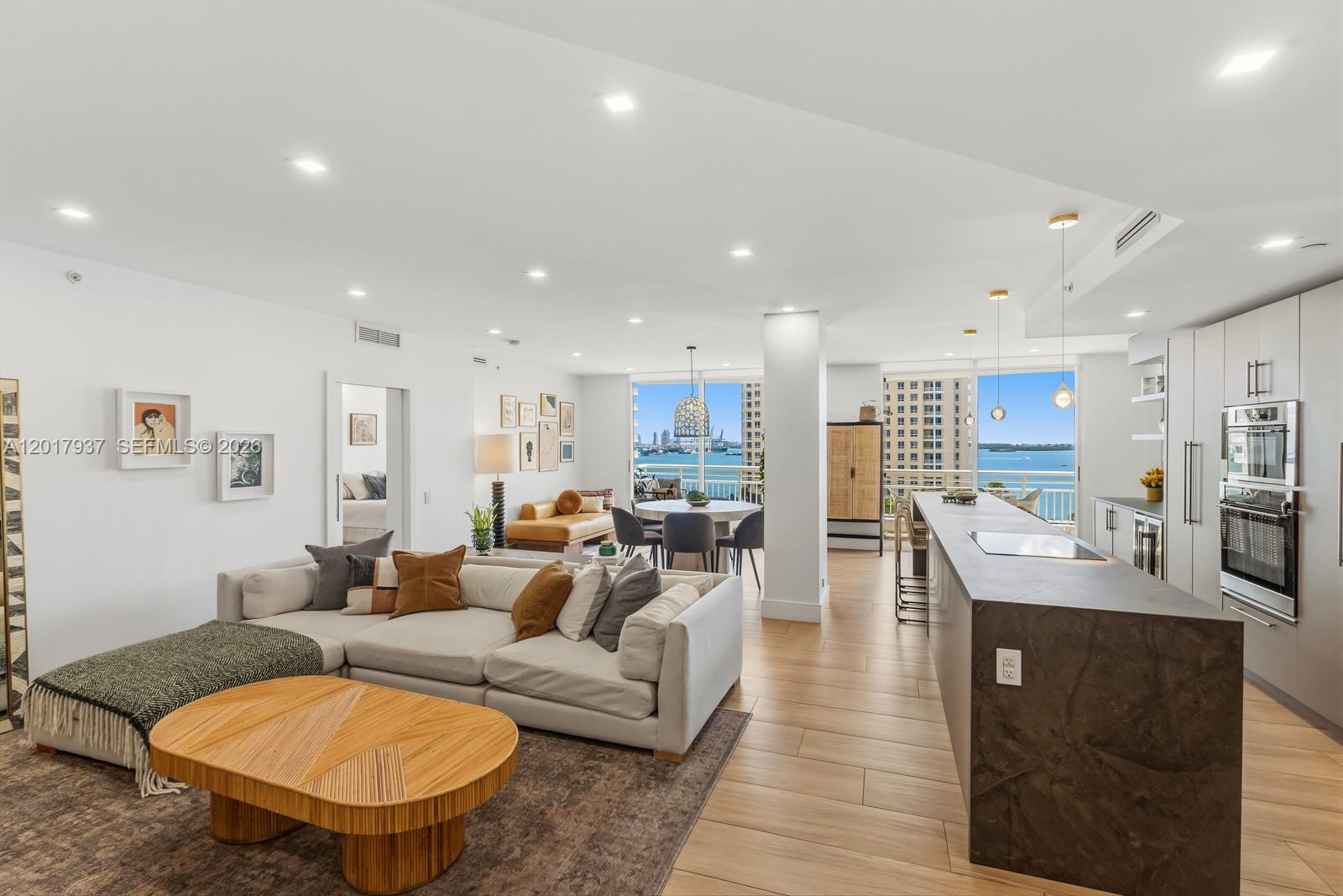 A modern open-concept living room and kitchen feature a large island and waterfront balcony views — 888 Brickell Key Dr # 1207, Miami FL 33131, MIAMI, FL
