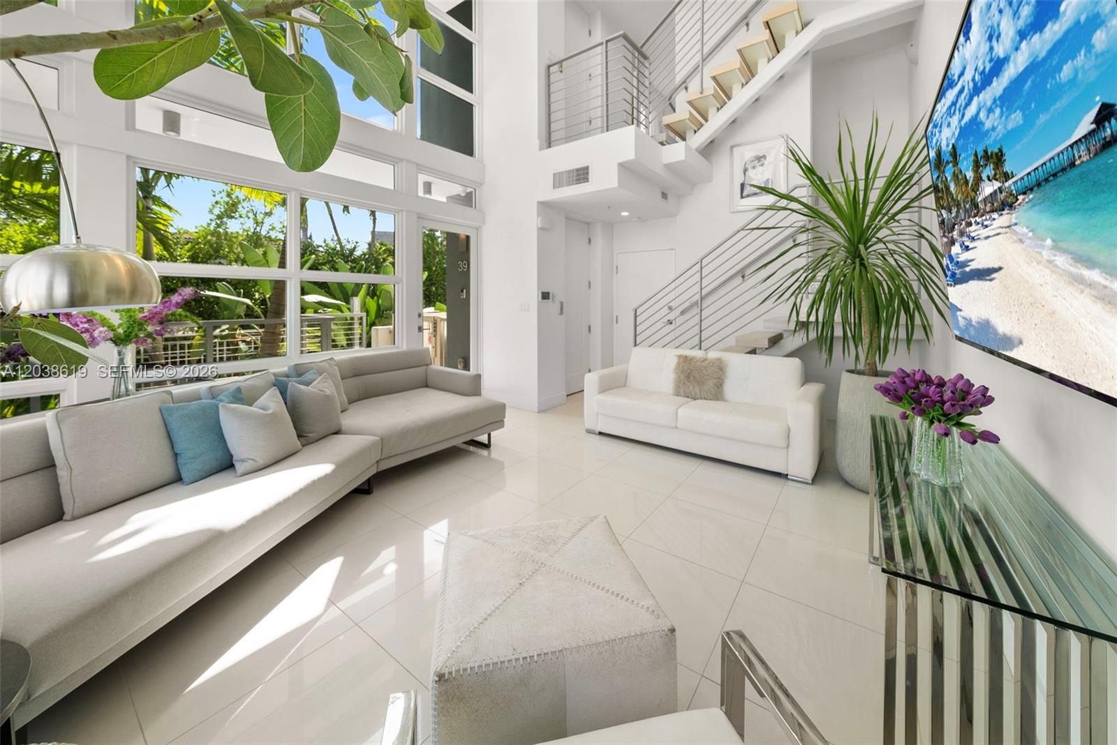 A bright, modern living room features high ceilings, large windows, white tile floors, and stairs — 39 N Shore Dr, Miami Beach FL 33141, MIAMI BEACH, FL