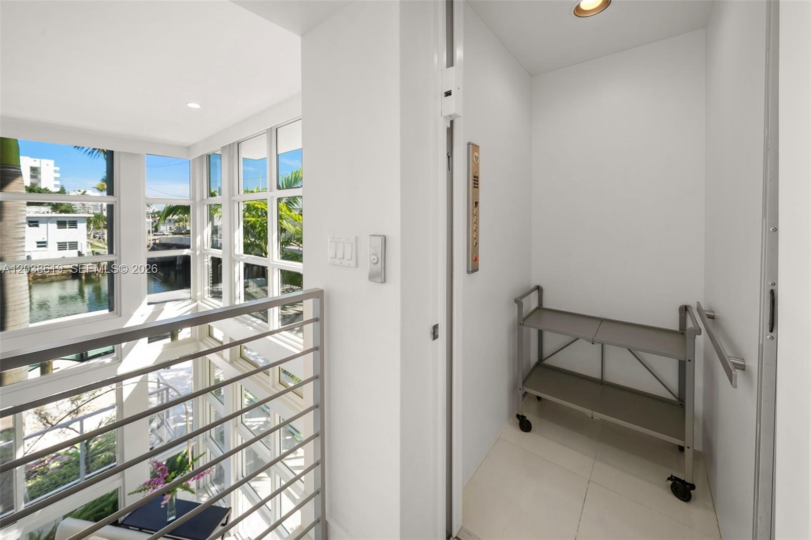 An elevator interior with a metal cart sits next to a windowed stairwell area — 39 N Shore Dr, Miami Beach FL 33141, MIAMI BEACH, FL