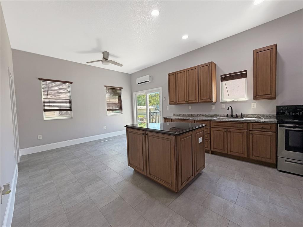 A kitchen features wood cabinets, a dark island, stainless steel appliances, and gray tile floors — 706 NEW YORK AVENUE, ST CLOUD, FL