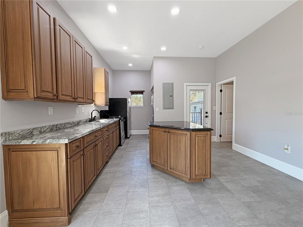 A kitchen features wood cabinets, granite countertops, a center island, and gray tile flooring — 706 NEW YORK AVENUE, ST CLOUD, FL