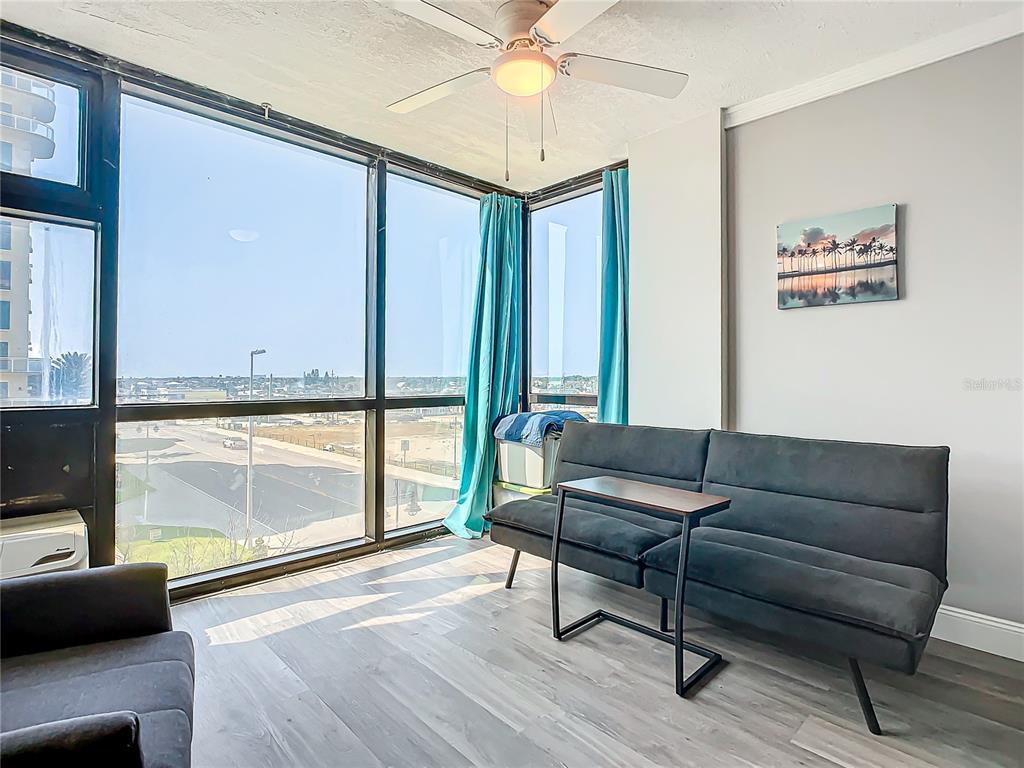 A sunroom features floor-to-ceiling windows, a ceiling fan, gray flooring, and a dark sofa — 1909 S ATLANTIC AVENUE UNIT 402, DAYTONA BEACH, FL