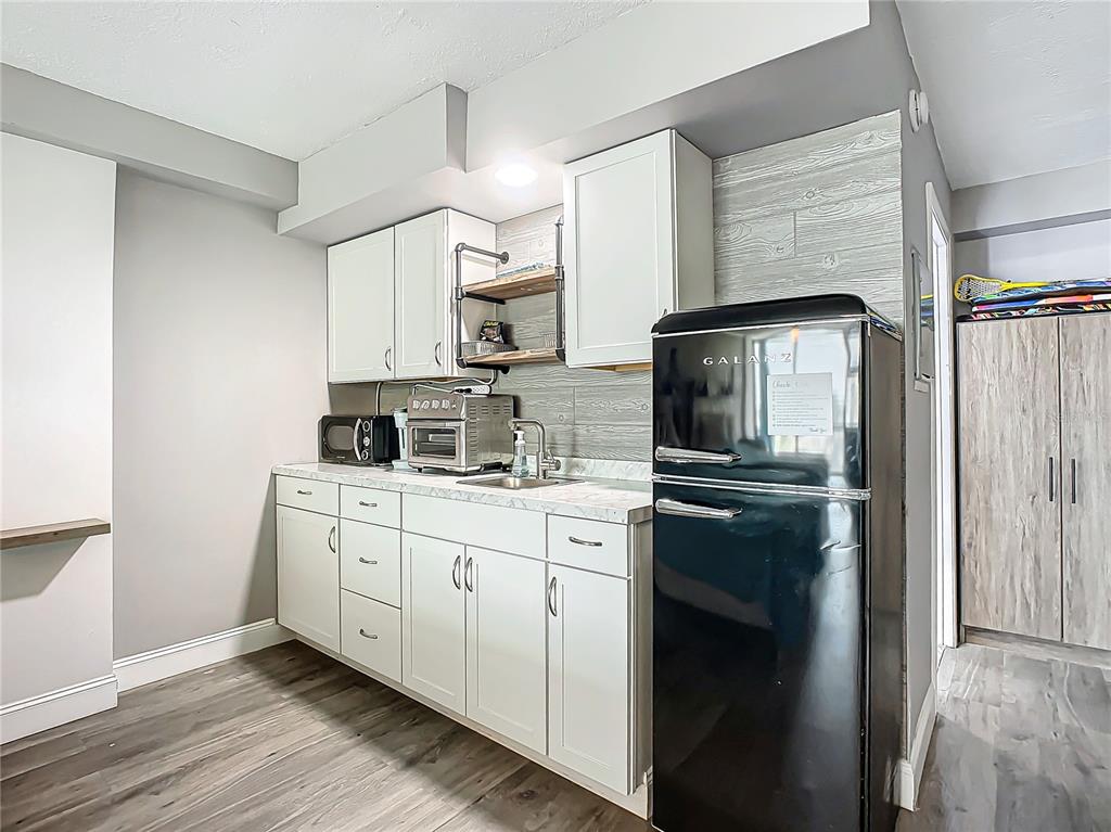 A small kitchen features white cabinets, a black retro-style refrigerator, and wood-look plank flooring — 1909 S ATLANTIC AVENUE UNIT 402, DAYTONA BEACH, FL
