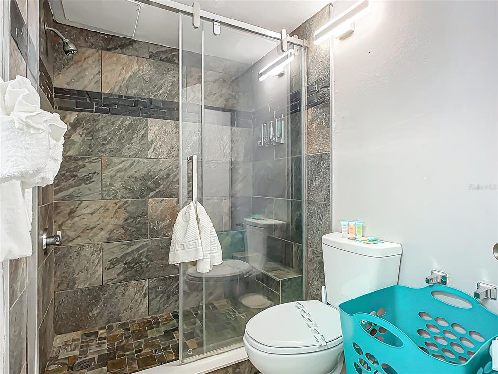 A bathroom features a glass-enclosed shower with stone tile walls and a white toilet — 1909 S ATLANTIC AVENUE UNIT 402, DAYTONA BEACH, FL