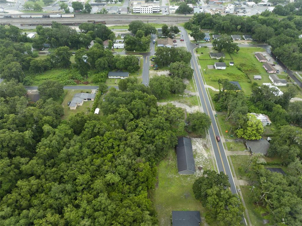 An aerial view shows a residential street with houses, dense trees, and a nearby railroad — 601 KILGORE STREET, WILDWOOD, FL
