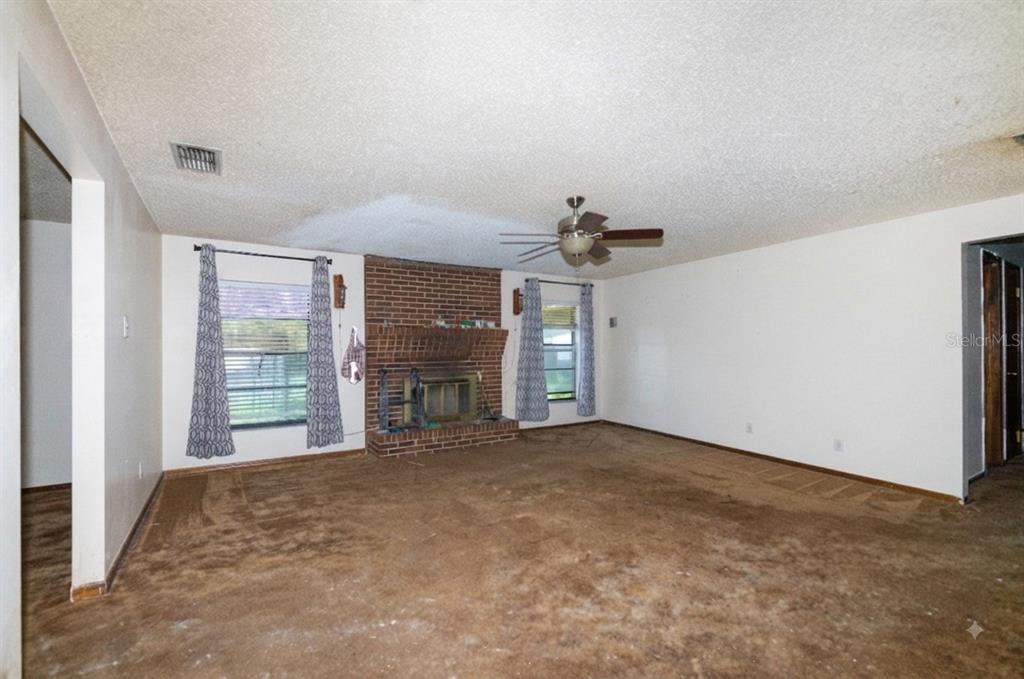 An empty living room features brown carpet, a brick fireplace, and a ceiling fan — 1723 BRANGUS DRIVE, LAKELAND, FL