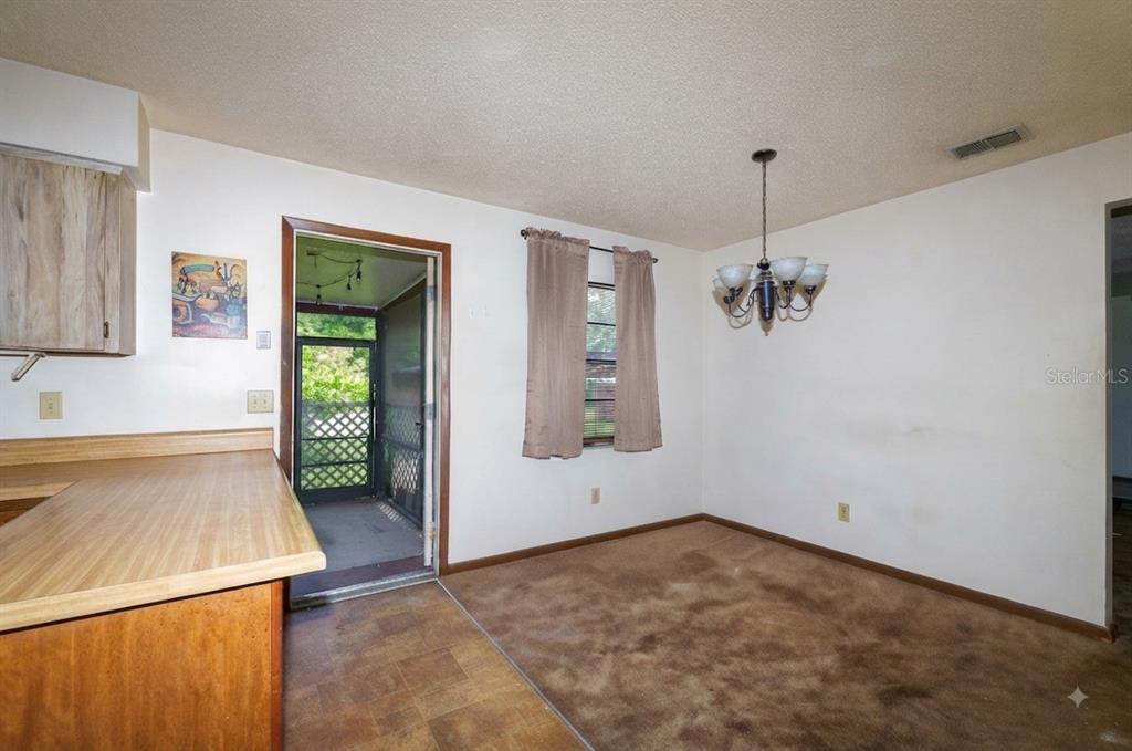 A dining area features brown carpeting, a chandelier, a window with curtains, and a screen door — 1723 BRANGUS DRIVE, LAKELAND, FL