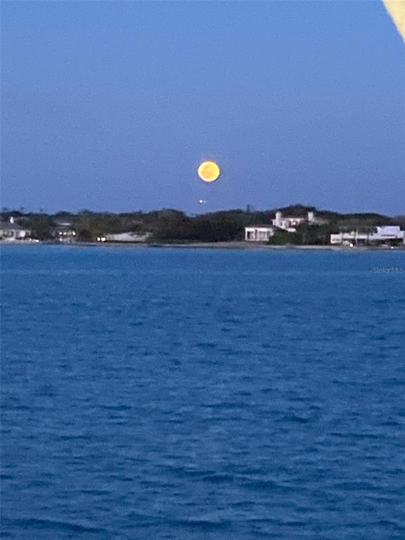 A full moon hangs over a body of water with houses visible on the distant shore — KACHER ROAD, NORTH PORT, FL