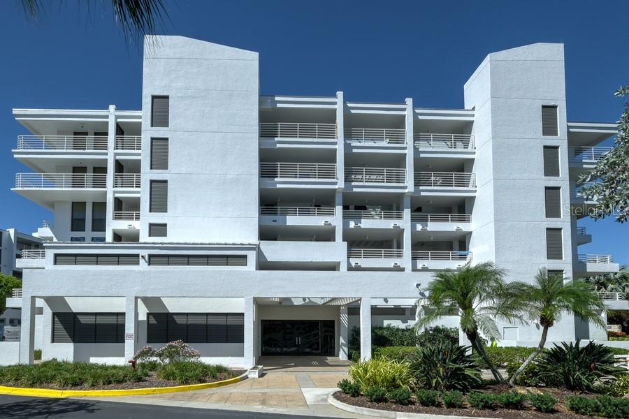 A multi-story white residential building with balconies and a ground-level entrance under a clear sky — 2105 GULF OF MEXICO DRIVE UNIT 3404, LONGBOAT KEY, FL