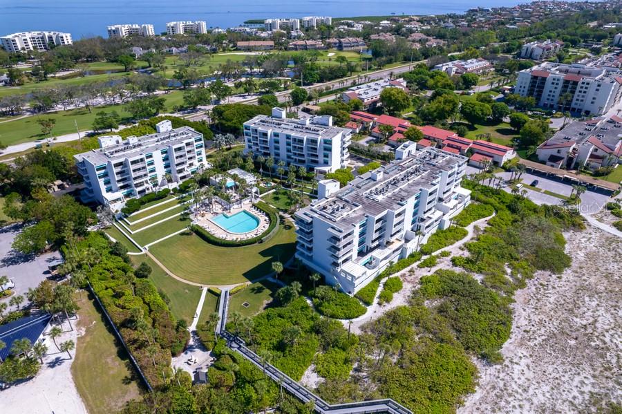 An aerial view shows multi-story apartment buildings, a swimming pool, and a boardwalk near the beach — 2105 GULF OF MEXICO DRIVE UNIT 3404, LONGBOAT KEY, FL