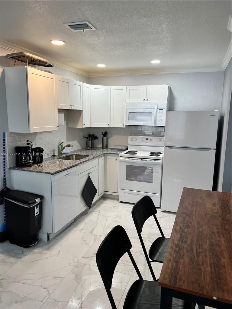 A kitchen features white cabinets, granite countertops, white appliances, and light-colored marble-patterned tile flooring — 2240 Simms St, Hollywood FL 33020, HOLLYWOOD, FL