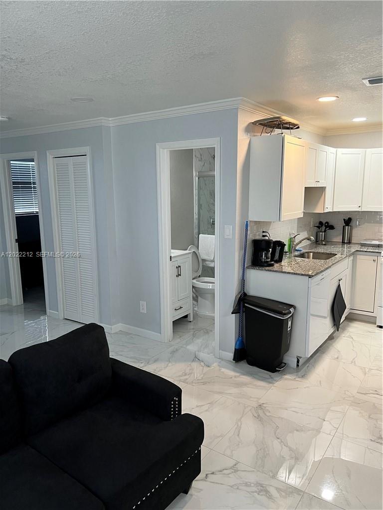 A kitchen with white cabinets and granite countertops opens into a living area with tile — 2240 Simms St, Hollywood FL 33020, HOLLYWOOD, FL