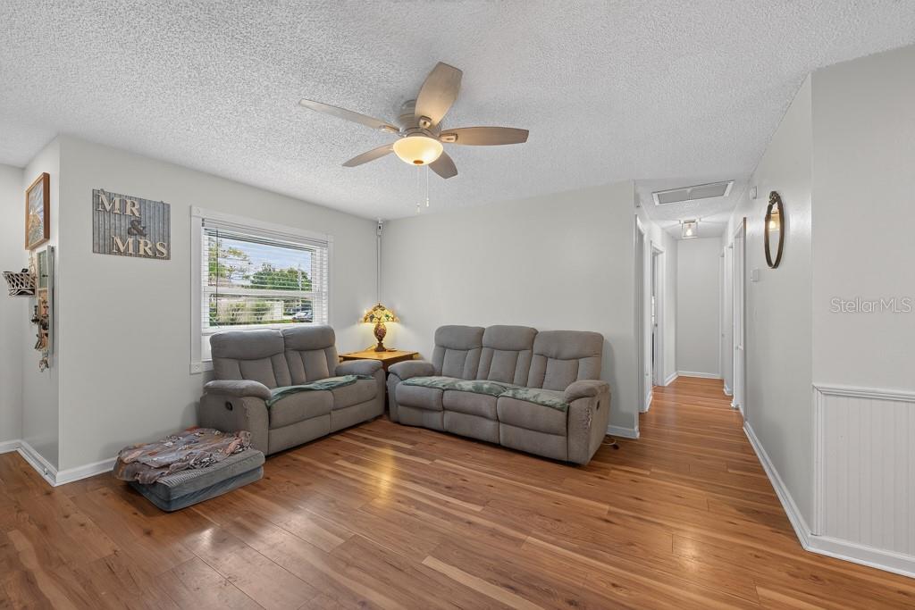 A living room features gray reclining sofas, wood flooring, and a ceiling fan — 6070 73RD STREET N, ST PETERSBURG, FL