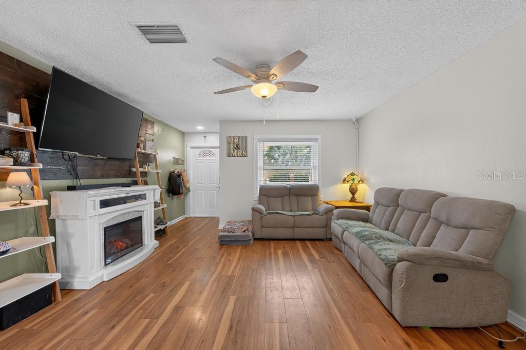 A living room features wood-look flooring, a fireplace, a television, and two gray sofas — 6070 73RD STREET N, ST PETERSBURG, FL
