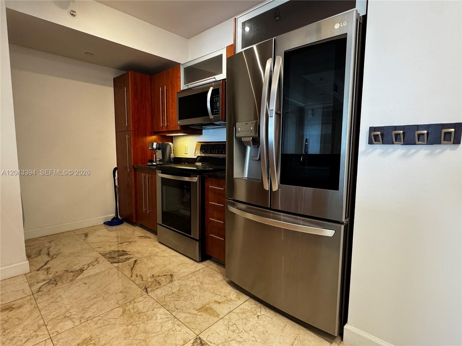 A kitchen features stainless steel appliances, wood cabinetry, and light-colored marble tile flooring — 7350 SW 89th St # 1809S, Miami FL 33156, MIAMI, FL