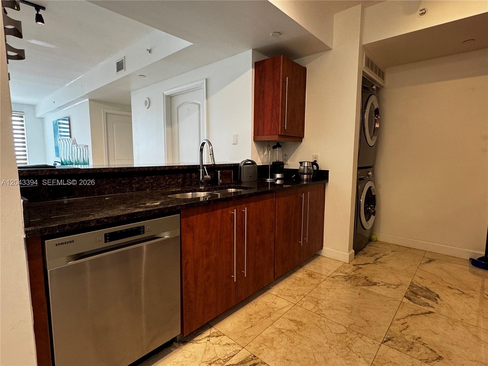 A kitchen features dark wood cabinets, granite countertops, stainless steel appliances, and a stacked washer-dryer — 7350 SW 89th St # 1809S, Miami FL 33156, MIAMI, FL