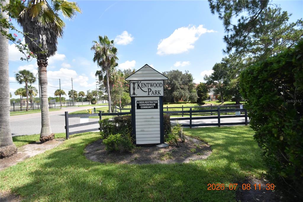 A sign for Kentwood Park condominium community stands in a grassy area with palm trees — 2302 MAKI ROAD UNIT 2, PLANT CITY, FL