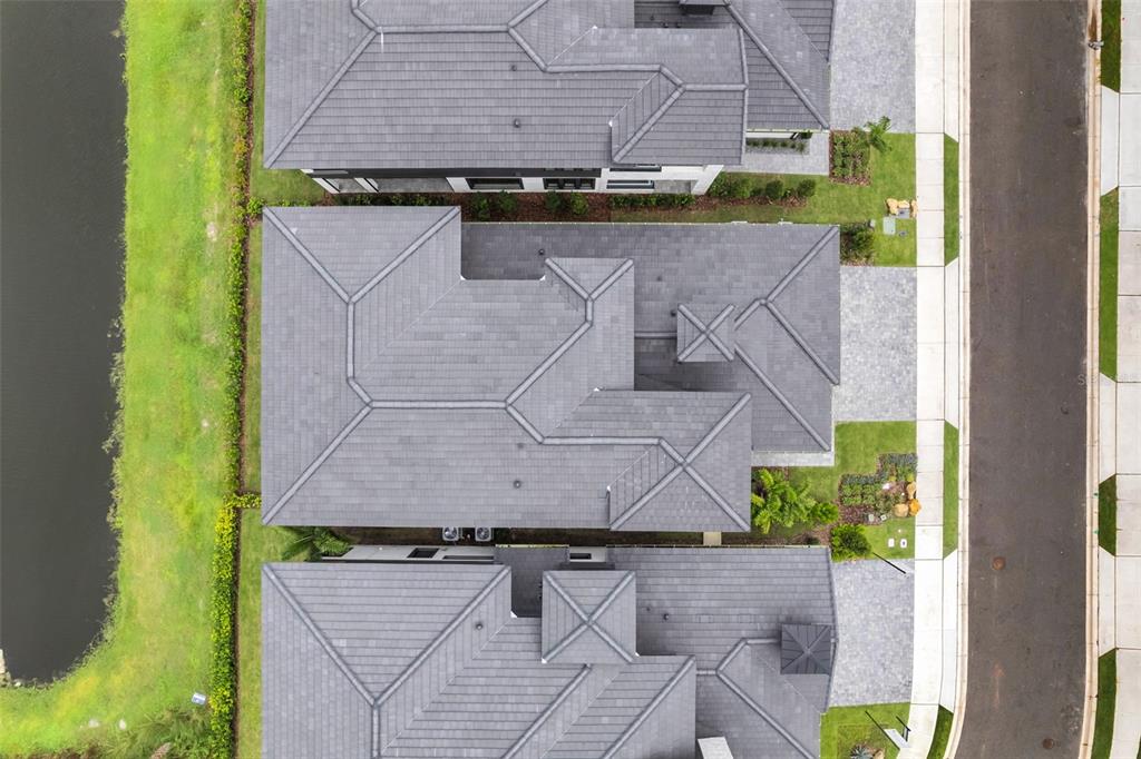 An aerial view shows the gray tiled roofs of three suburban homes beside a pond — 3015 KENSINGTON AVENUE, DAVENPORT, FL