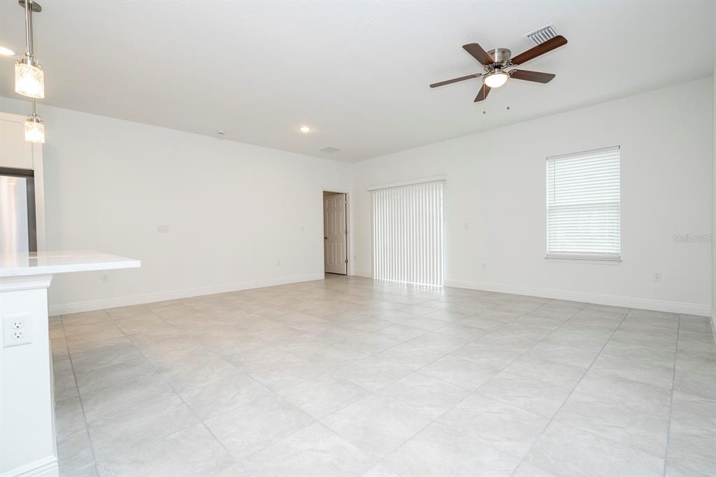 A spacious room with white walls, light tile flooring, a ceiling fan, and sliding glass doors — 17298 SW 36TH AVENUE ROAD, OCALA, FL