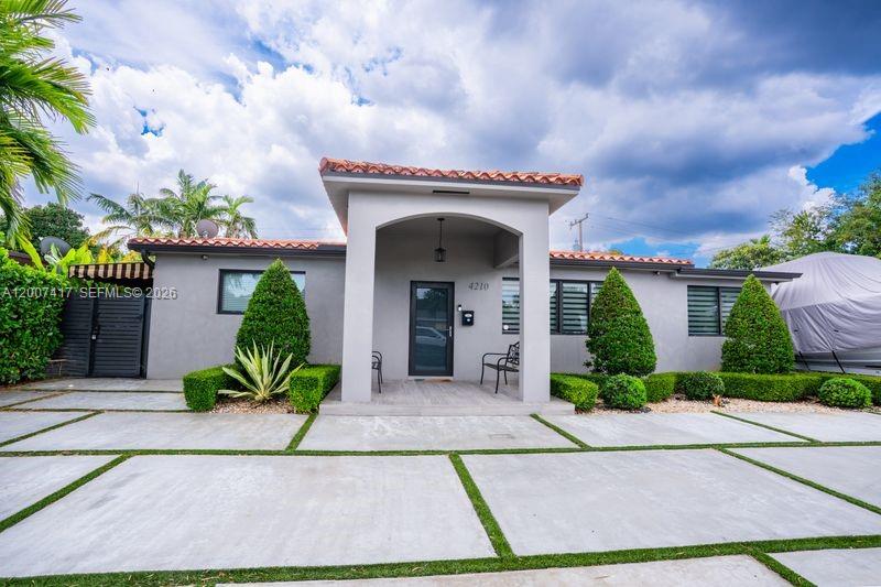 A gray single-story house features a covered entryway, a tiled roof, and a concrete driveway — 4210 W 6th Ave, Hialeah FL 33012, HIALEAH, FL