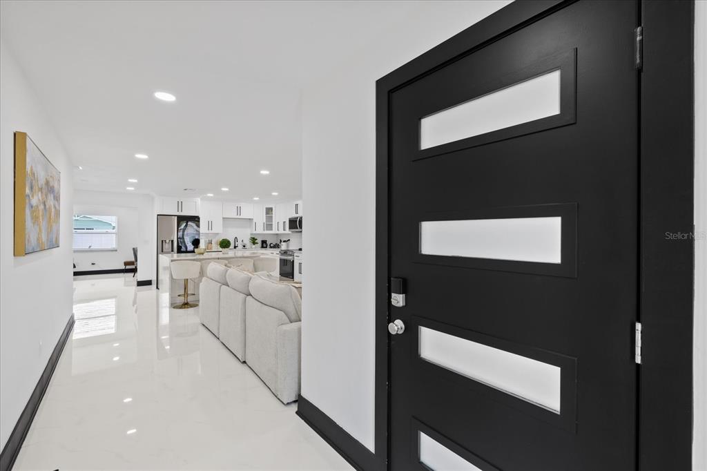 A black front door with glass panels opens into a bright, white-tiled open-concept living area — 2461 69TH AVENUE S, ST PETERSBURG, FL