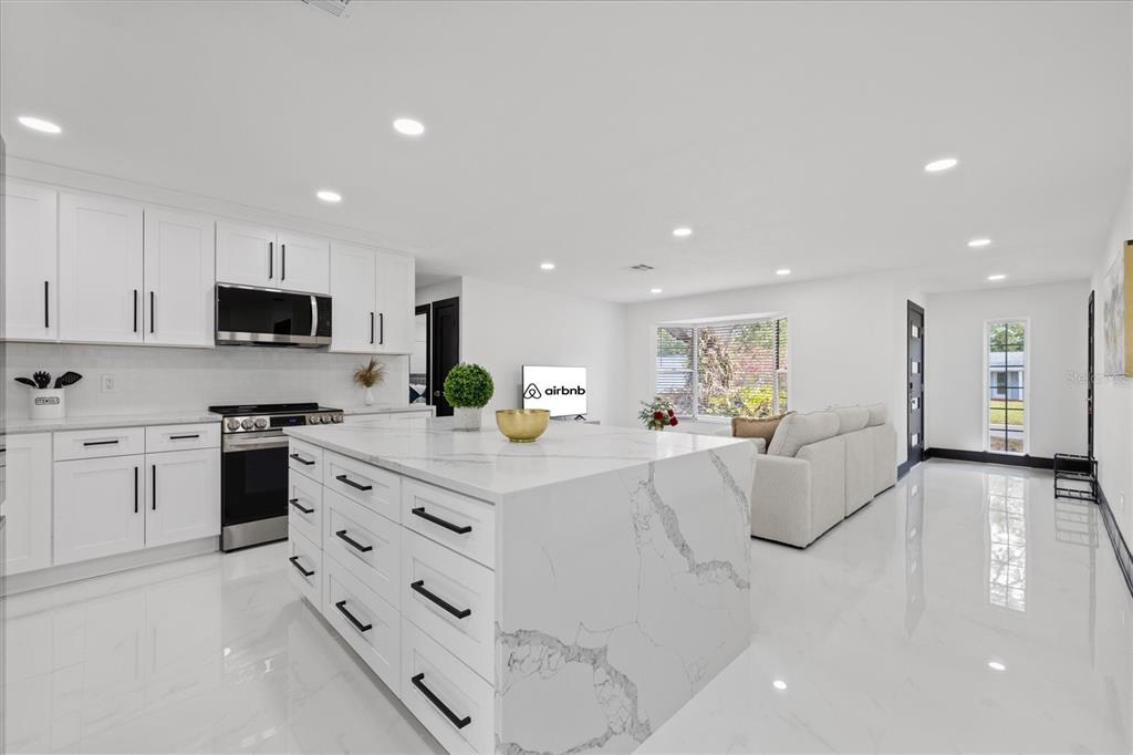 A modern kitchen with a large marble island, white cabinets, and an open-concept living area — 2461 69TH AVENUE S, ST PETERSBURG, FL