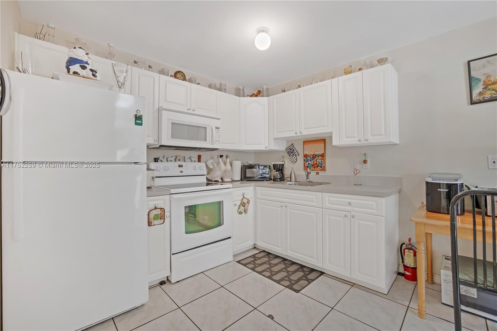 A kitchen features white cabinets, white appliances, light countertops, and light-colored tile flooring — 265 NE 12th Ave # 265, Homestead FL 33030, HOMESTEAD, FL