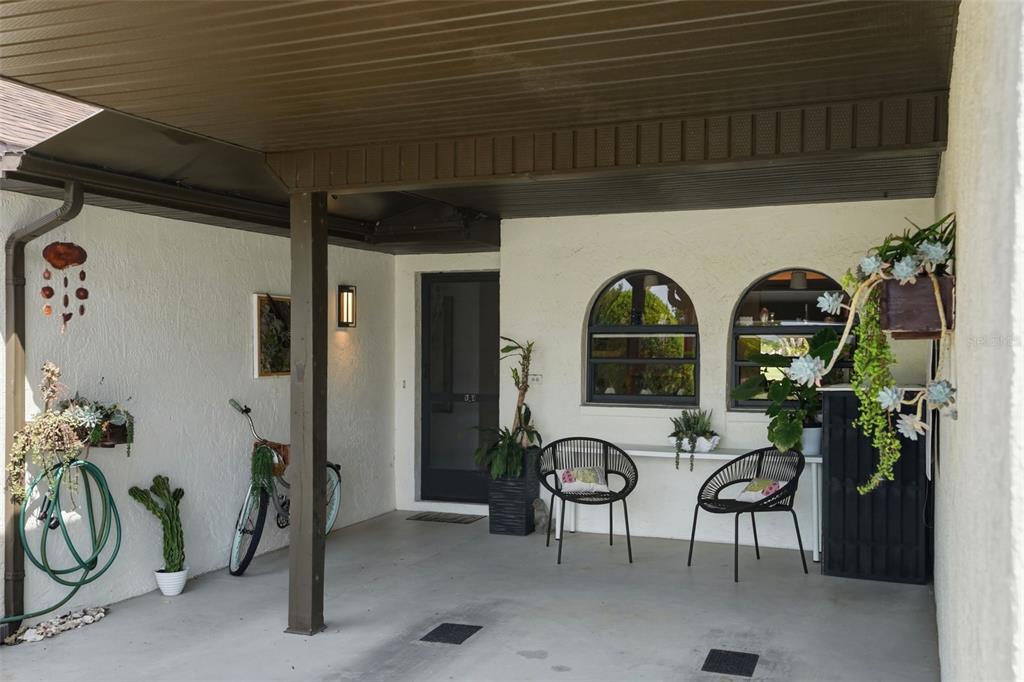 A covered patio features a concrete floor, two black chairs, a bicycle, and potted plants — 9143 LINGROVE ROAD, WEEKI WACHEE, FL