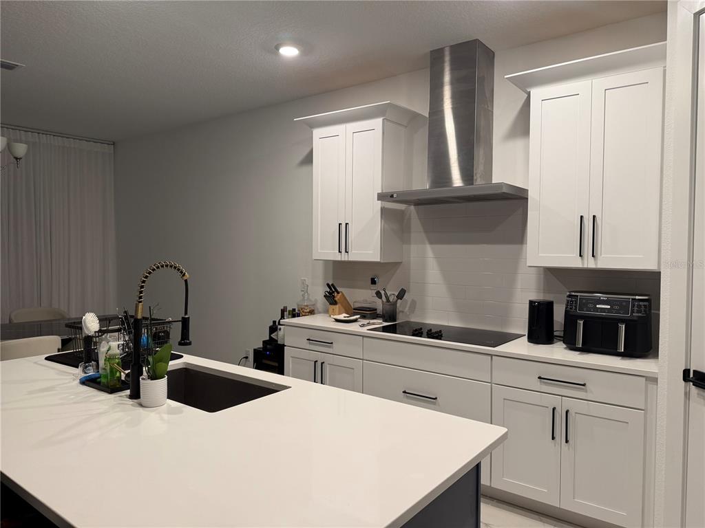 A modern kitchen features white cabinetry, a large island with a sink, and stainless appliances — 2252 GOLD SUMMIT STREET, MINNEOLA, FL