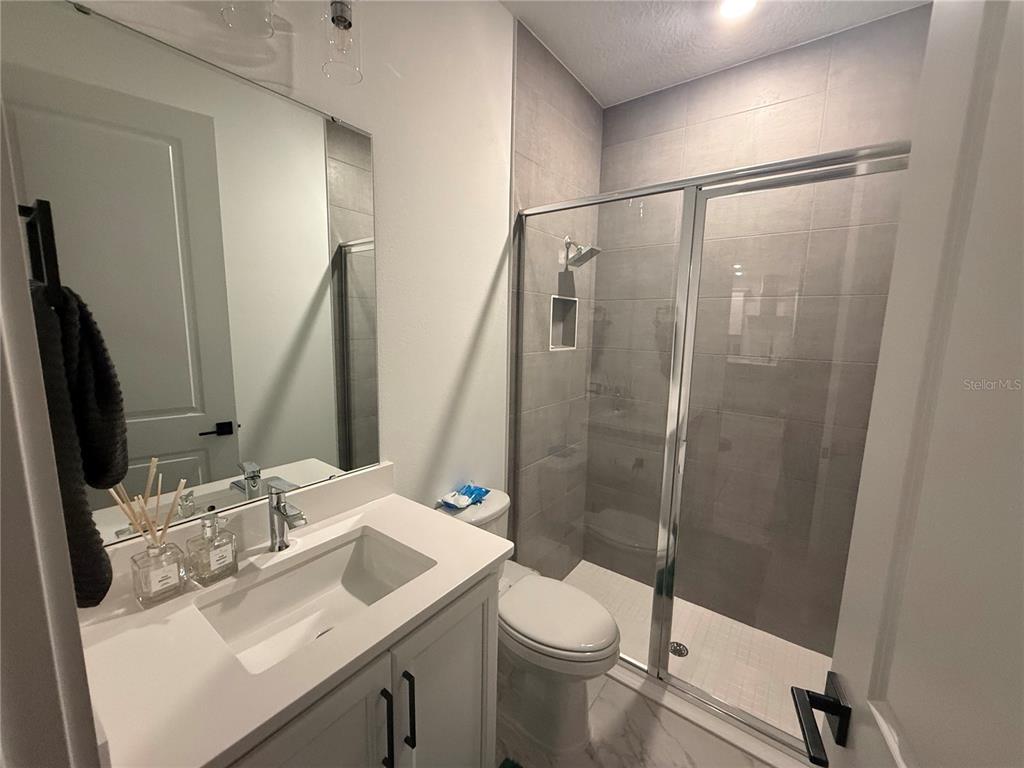 A bathroom features a white vanity, a toilet, and a glass-enclosed tiled shower — 2252 GOLD SUMMIT STREET, MINNEOLA, FL