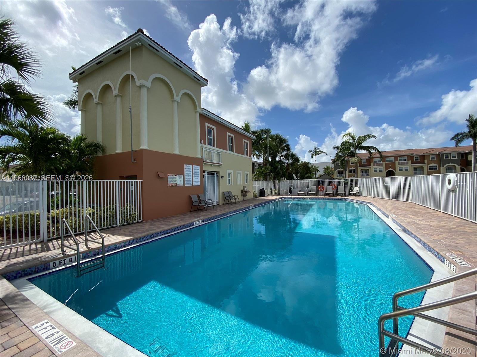 A rectangular outdoor swimming pool is surrounded by a white fence and a multi-story building — 8899 NW 107 CT # 12, Doral FL 33178, DORAL, FL