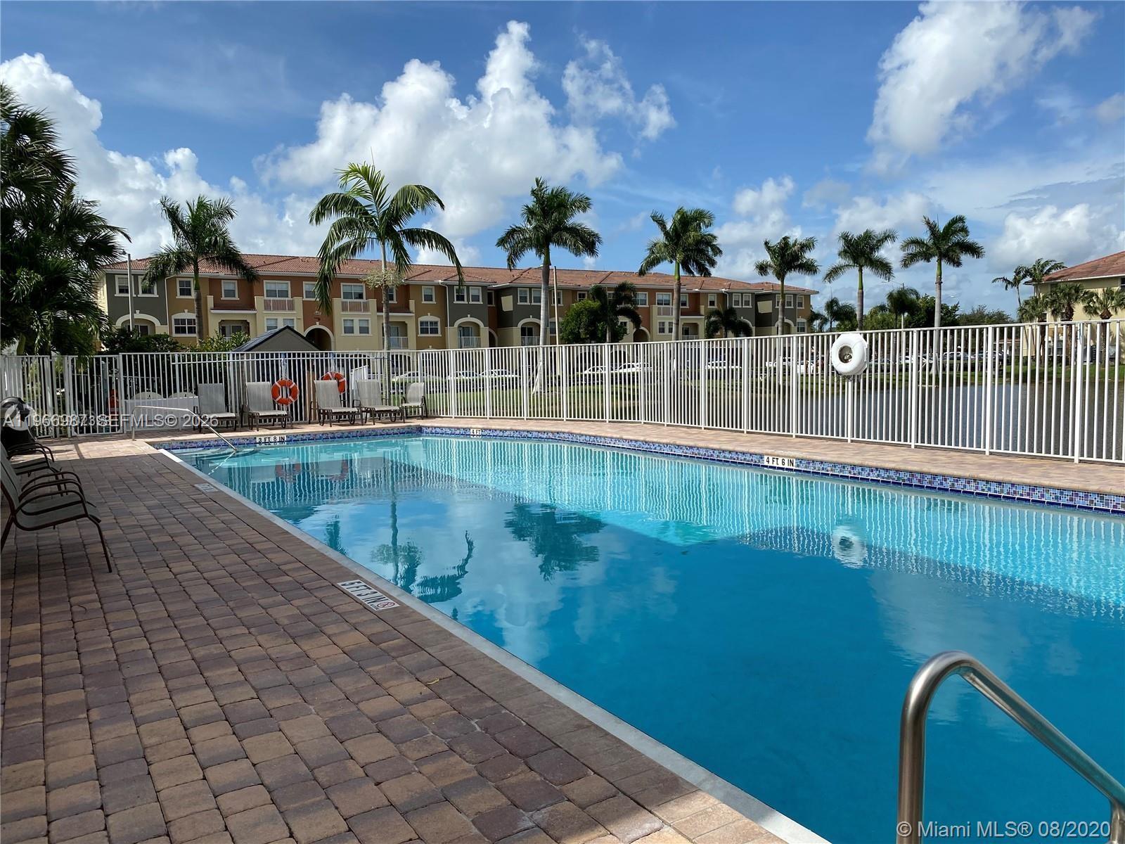 A swimming pool with a brick deck is enclosed by a white fence near apartment buildings — 8899 NW 107 CT # 12, Doral FL 33178, DORAL, FL