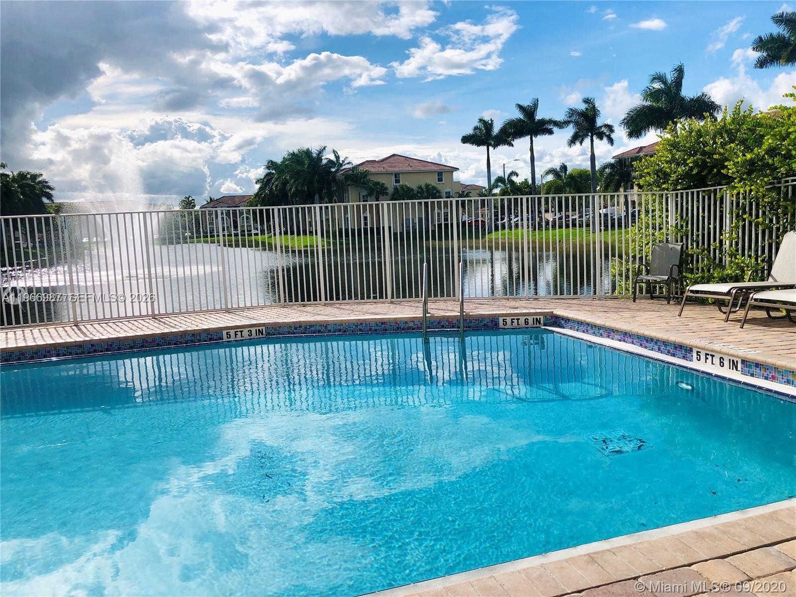 A swimming pool with depth markers overlooks a lake and a fountain behind a fence — 8899 NW 107 CT # 12, Doral FL 33178, DORAL, FL