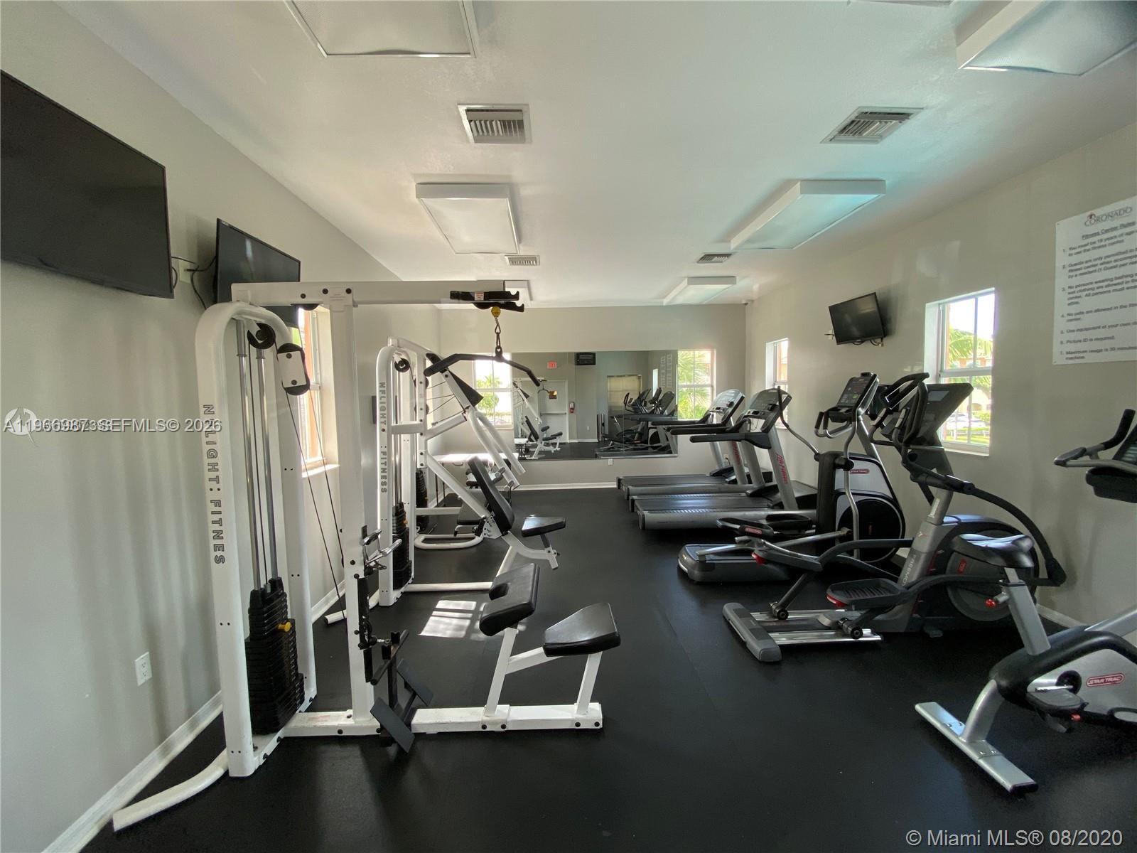 A fitness center features a multi-station weight machine, several treadmills, and elliptical trainers on black flooring — 8899 NW 107 CT # 12, Doral FL 33178, DORAL, FL