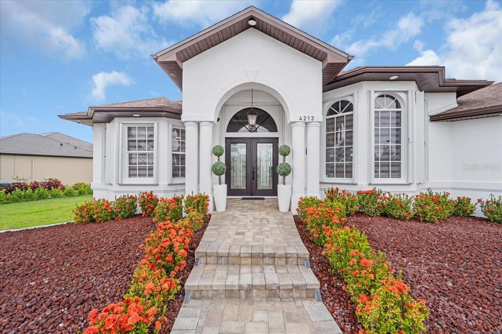A white house with a stone walkway, arched entryway, and red mulch landscaping — 4213 NW 28TH STREET, CAPE CORAL, FL