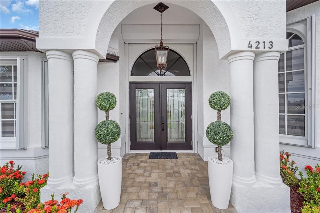 A front entryway features a double door, arched transom window, and two potted topiary plants — 4213 NW 28TH STREET, CAPE CORAL, FL